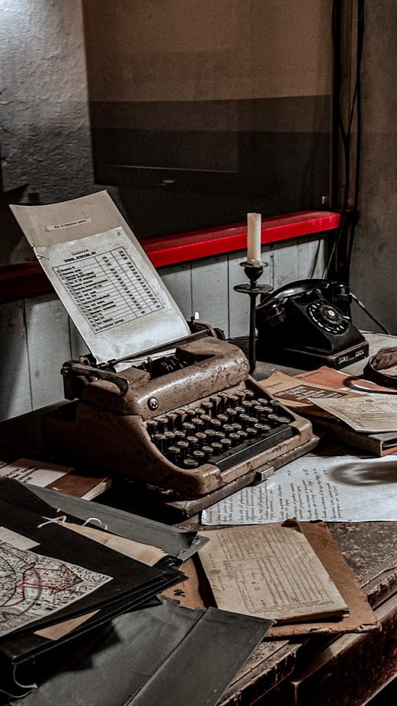 A nostalgic desk setup featuring an old typewriter, papers, and candlestick.