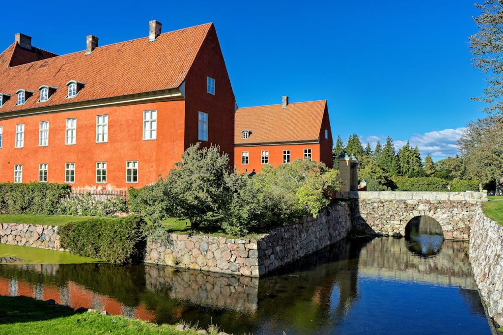 A beautifully preserved historic estate in Skåne län, Sweden, with a picturesque bridge and canal under clear blue skies.