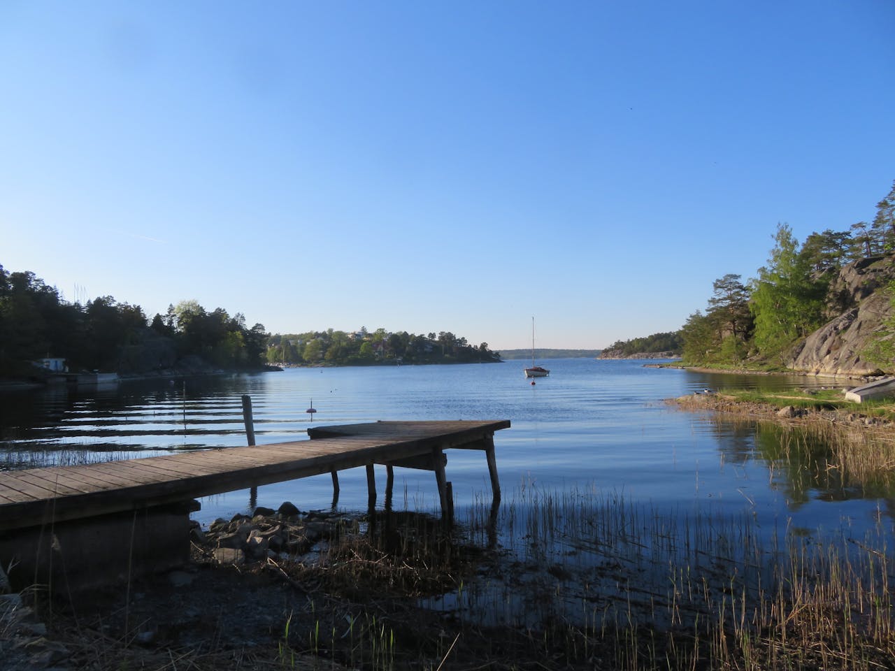 Peaceful lakeside scene featuring a wooden dock and calm waters under a clear blue sky.